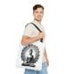 A person in a light shirt and jeans carries the Buddha Tote Bag (AOP), showcasing a stylish design of a meditating Buddha with a sunburst.