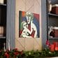 The Mother's Love Cubism Art Canvas, inspired by Picasso's cubism style, showcases abstract human figures and is mounted on a wooden wall. Shelves holding books and red candles complement the canvas on either side, while a garland adorns its lower edge.