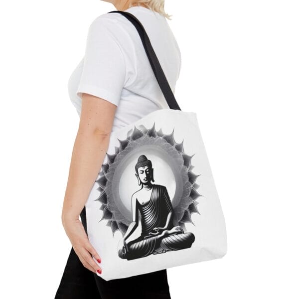 A person holding the Buddha Tote Bag (AOP), featuring a black and white illustration of a seated Buddha surrounded by an intricate circular pattern. A person holding the Buddha Tote Bag (AOP), featuring a black and white illustration of a seated Buddha surrounded by an intricate circular pattern.