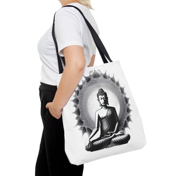 Person holding a Buddha Tote Bag (AOP) featuring a black and white illustration of a seated Buddha in a lotus position, encircled by an elegant floral design. Person holding a Buddha Tote Bag (AOP) featuring a black and white illustration of a seated Buddha in a lotus position, encircled by an elegant floral design.