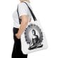 Person holding a Buddha Tote Bag (AOP) featuring a black and white illustration of a seated Buddha in a lotus position, encircled by an elegant floral design.