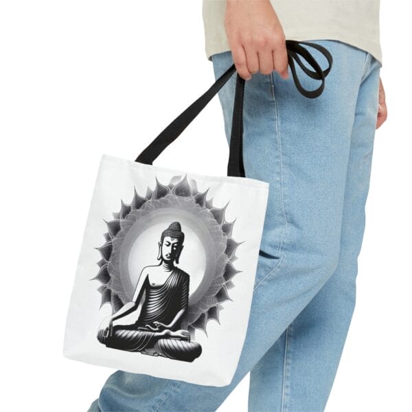 A person holds a Buddha Tote Bag (AOP), featuring a white design with a black and white image of Buddha in a meditative pose, surrounded by an intricate mandala. This chic accessory beautifully embodies the blend of serenity and style found in Buddha tote handbags. A person holds a Buddha Tote Bag (AOP), featuring a white design with a black and white image of Buddha in a meditative pose, surrounded by an intricate mandala. This chic accessory beautifully embodies the blend of serenity and style found in Buddha tote handbags.