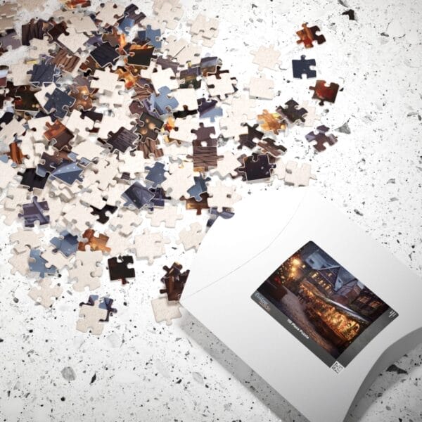The scattered pieces of the Christmas Night Puzzle, depicting a completed winter village scene on the box lid, rest on a speckled surface. The scattered pieces of the Christmas Night Puzzle, depicting a completed winter village scene on the box lid, rest on a speckled surface.